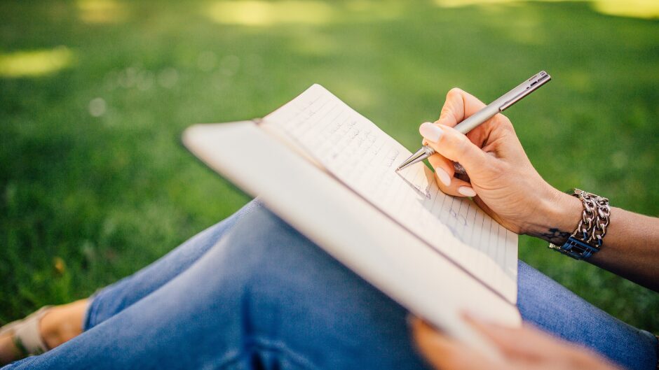 芝生の上でノートを書く女性