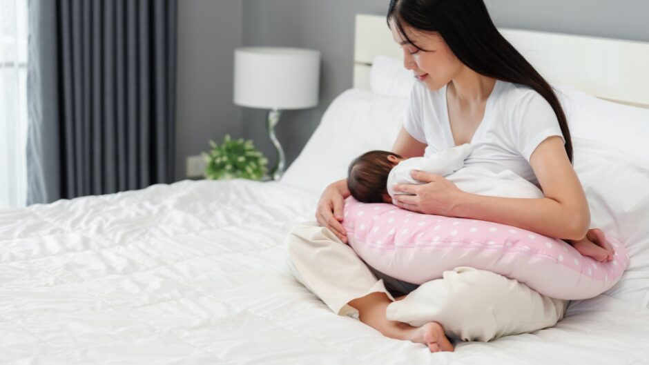 ベットの上で授乳クッションを使用して授乳をする女性